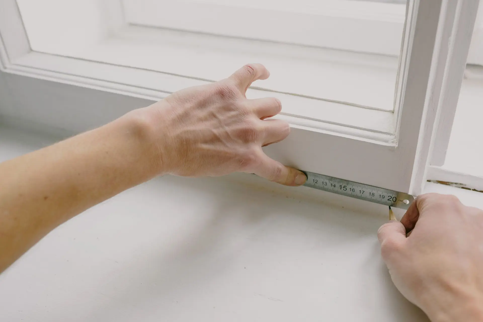 Manos midiendo con cinta métrica el marco de una ventana de madera
